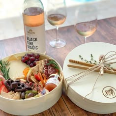 a wine bottle and some food on a table next to a bowl with grapes in it