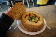 a person holding a piece of bread over a bowl filled with food on a plate