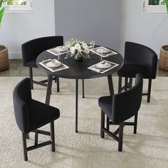 a round table with black chairs and white plates on it in front of a potted plant