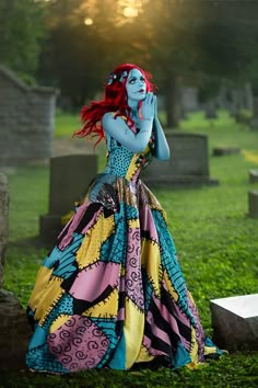 a woman with red hair and blue skin wearing a colorful dress standing in the grass