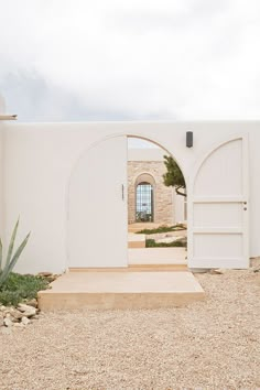 an open door leading to a white building with a cactus in the foreground and rocks on the ground