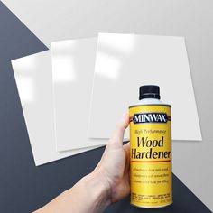 a hand holding a can of wood hardener next to three sheets of white paper