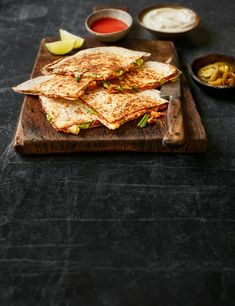 quesadillas on a cutting board with dipping sauces