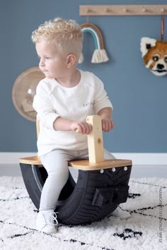 a little boy sitting on top of a wooden toy boat in a room with blue walls