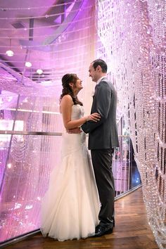 a bride and groom standing next to each other in front of a purple curtain with beads