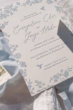 a close up of a wedding card on top of a bed with white sheets and blue ribbon