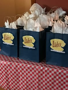 three bags with the words luke's on them are sitting on a red and white checkered tablecloth