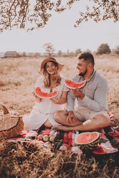 a man and woman sitting on a blanket eating watermelon