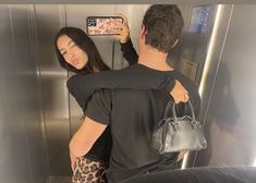 a man and woman standing in front of an elevator taking pictures with their cell phones