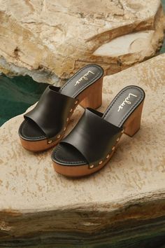 The Lulus Jaylani Black Platform Mule Sandals are the perfect combination of cute and cool for all your warm weather 'fits! Smooth faux leather shapes these essential sandals that have an almond footbed and a wide vamp strap with shiny gold stud accents along the side, all atop a 1.25"" toe platform. Easy slide-on design makes for effortless, everyday styling, while a sturdy wood-look block heel completes the classic clog-inspired look! 3. 75" wood-look block heel. Lightly cushioned insole. Rubb Chic Synthetic Clogs With Open Heel, Chic Sandals With Wooden Heel, Chic Clogs With Wooden Heel For Beach, Summer Leather Clogs With Padded Heel, Chic Beach Clogs With Wooden Heel, Chic Block Heel Clogs For The Beach, Chic Beach Clogs With Block Heel, Chic Open Toe Clogs With Cushioned Footbed, Chic High Heel Clogs For Beach