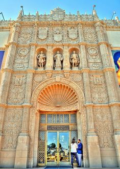 two people are standing in front of an ornately designed building with statues on it