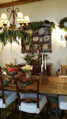 a wooden table topped with lots of white chairs next to a wall mounted shelf filled with christmas wreaths