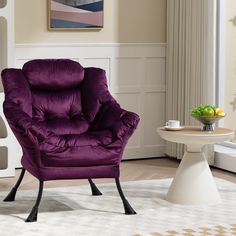 a purple chair sitting in a living room next to a white table with a vase on it