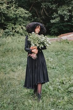 a woman standing in the grass holding flowers