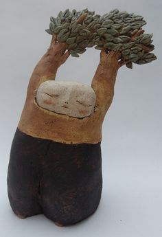 a ceramic sculpture of a person holding a tree with their head in the air and sleeping on it