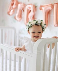 the baby is smiling in her crib with balloons hanging from it's ceiling