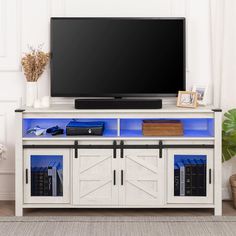 a flat screen tv sitting on top of a white entertainment center next to a potted plant