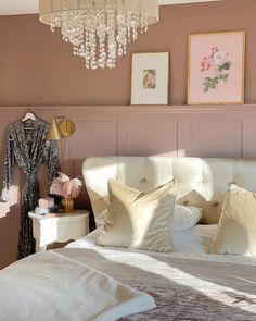 a white bed sitting under a chandelier next to a wall with pictures on it