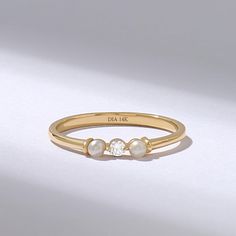 a gold ring with two pearls on the side and a diamond in the middle, sitting on a white surface