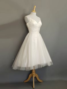 a short white dress on a mannequin stand with a gray wall in the background