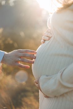 a pregnant woman is touching her husband's hand with the sun shining in the background