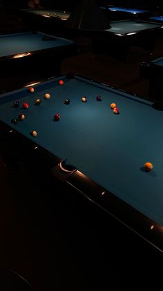 several pool tables with balls on them in a dark room, one is blue and the other is black