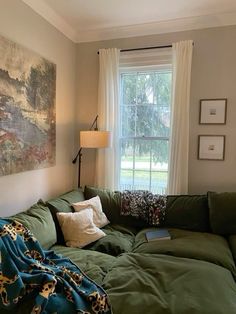 a green couch sitting in front of a window next to a painting on the wall