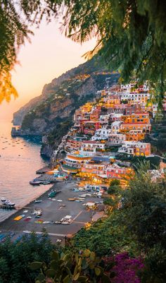 the sun is setting over an ocean and some boats are parked on the shore in front of houses