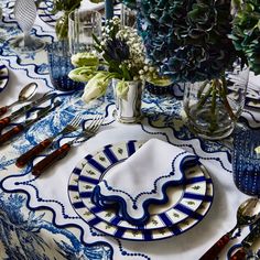 a blue and white table setting with flowers in vases on the top, silverware at the bottom