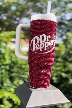 a red and white drink cup sitting on top of a metal stand in front of some bushes