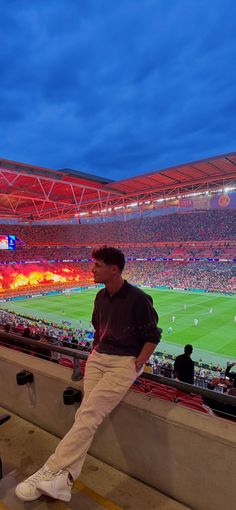 a man sitting on the edge of a stadium watching a soccer game at night time