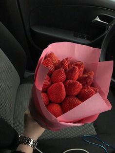 a person holding a pink paper bag full of strawberries in their hand while sitting in the back seat of a car