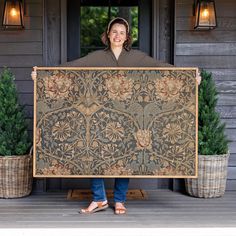 a woman holding up a large piece of art in front of a house with potted plants