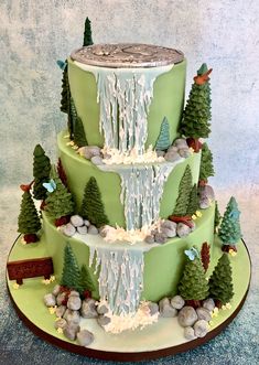 a three tiered cake decorated with trees, rocks and water pouring from the top