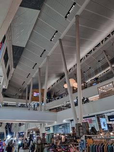 the inside of a shopping mall with lots of clothes on display and people walking around