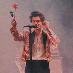 a man holding a rose up to his ear while standing in front of a microphone