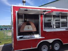 a red food truck parked in front of a building with an oven on it's side