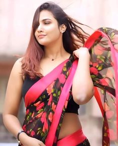 a woman wearing a black and pink sari with red flowers on it, posing for the camera