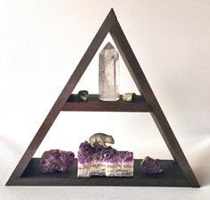 a triangle shaped shelf with rocks and a candle on it, in front of a white wall