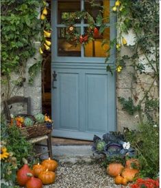 a blue front door with pumpkins and gourds in the garden next to it