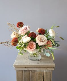 a vase filled with lots of flowers on top of a wooden table next to a wall