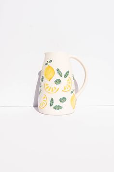 a ceramic pitcher with lemons and leaves painted on the side, sitting on a white surface