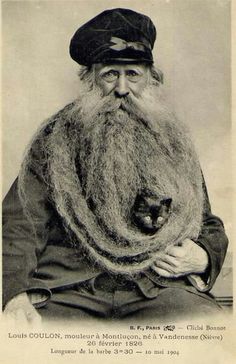 an old photo of a man with a long beard holding a cat in his lap