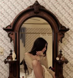 a woman sitting in front of a mirror on top of a dresser next to a wall