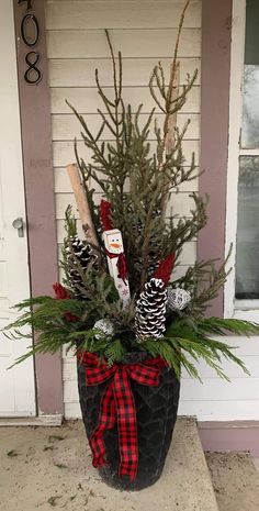 a potted plant with pine cones and evergreen branches in it on the front porch