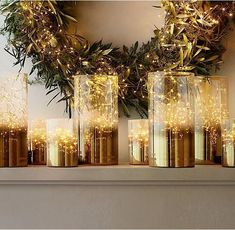 several vases with lights in them sitting on a shelf next to a christmas wreath