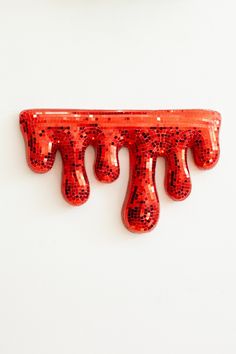 an orange wall hanging with red sequins on it's sides and three drops of water coming out of the top