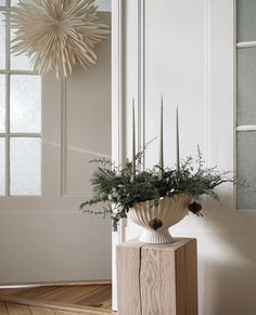 a vase filled with greenery sitting on top of a wooden table next to a door