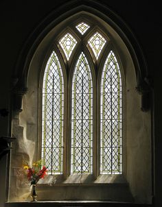 a vase filled with flowers sitting in front of a stained glass window on top of a stone wall