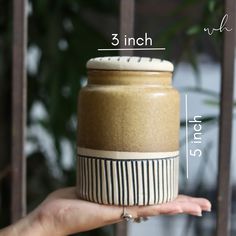 a hand holding a brown and white jar with measurements for the top half of it